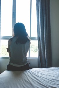 woman sitting on bed in room with light from window (abuse concept)