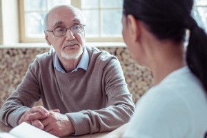 Watching you. Concentrated gray-haired male person holding hands together and being deep in thoughts